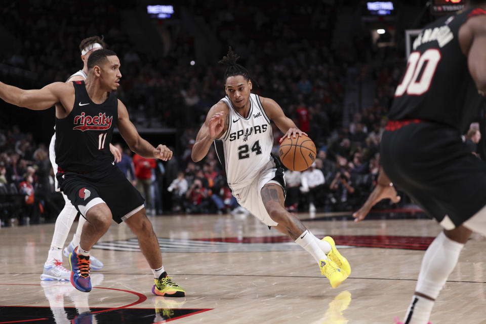 San Antonio Spurs guard Devin Vassell, middle, drives against Portland Trail Blazers guard Malcolm Brogdon, left, during the second half of an NBA basketball game Friday, Dec. 29, 2023, in Portland, Ore. (AP Photo/Howard Lao)