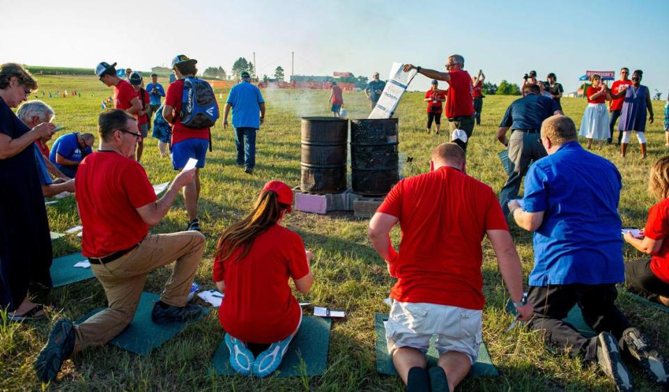 Attendees from across the U.S. and event leaders pray over names on cards, Friday, July 22, 2021, at the Prayer at the Heart of America event in Lebanon, Kansas., The cards were burned after the names were prayed for during the symbolic offering by fire at the end of the event.