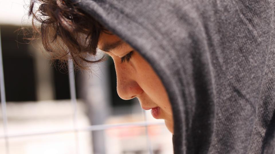 Sad troubled hispanic school boy teenager wearing a hoodie posing outdoor - close up stock photo.
