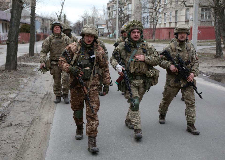 Armed Ukrainian troops walking down a narrow road.