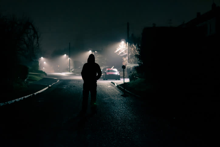 Silhouetted person standing in a dimly lit street at night, with streetlights in the background