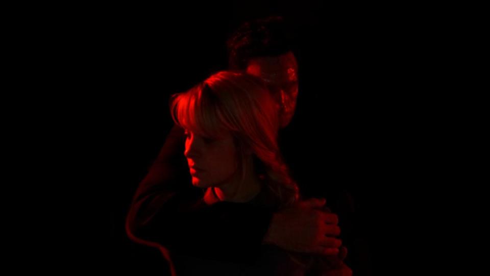 Brea Grant's May is embraced by a stalker stranger and drenched in red light in a still from the Shudder horror film Lucky.