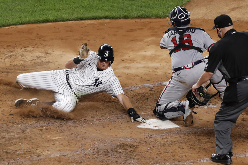 New York Yankees DJ LeMahieu, left, scores on Aaron Hick's fourth-inning double as Atlanta Braves catcher Travis d'Arnaud, center, waits for the throw in a baseball game, Wednesday, Aug. 12, 2020, in New York. Home plate umpire Todd Tichenor watches the play at right. (AP Photo/Kathy Willens)