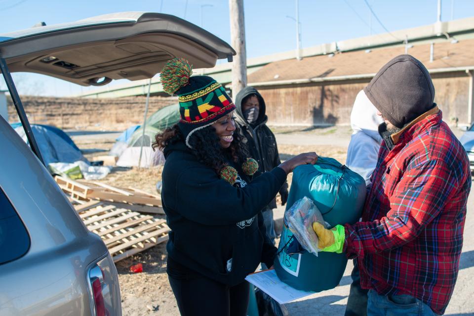 Tamika Sellars, team leader at Valeo, hands a sleeping bag and other supplies to a man living in a tent north of the Kansas River.