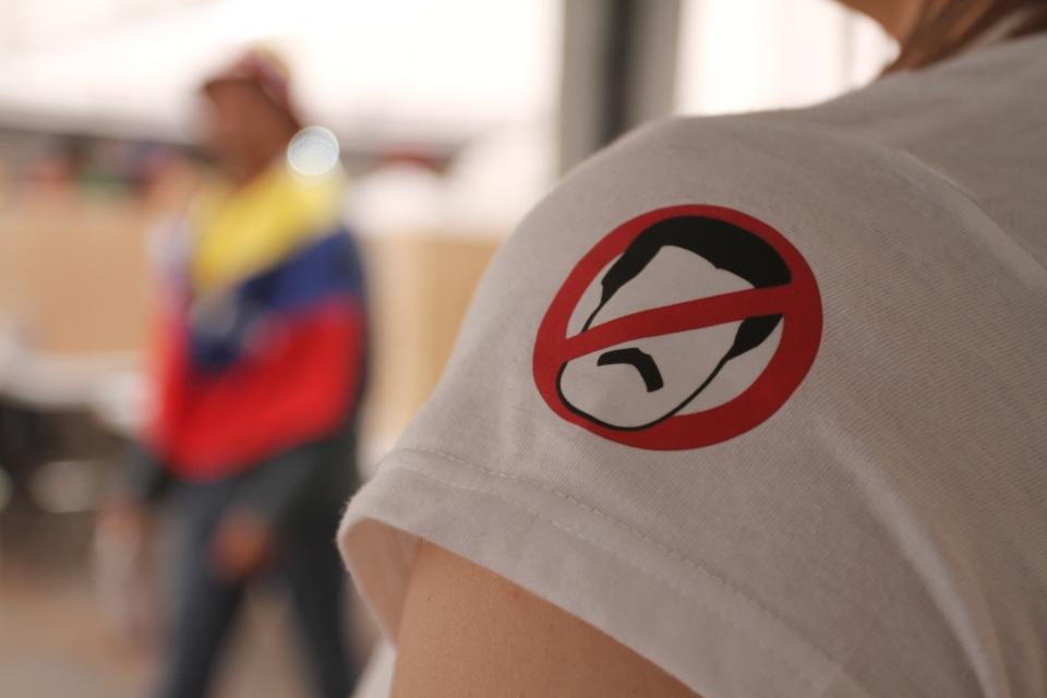 <p>Eine Frau im kolumbianischen Bogotá trägt ein T-Shirt mit einem Verbotszeichen, auf dem das Gesicht des venezolanischen Präsidenten Nicolás Maduro zu sehen ist. In Kolumbien haben Anhänger der venezolanischen Opposition an einem inoffiziellen Volksentscheid gegen Maduros Pläne für eine Verfassungsreform teilgenommen. (Bild: Sofia Toscano/colprensa/dpa) </p>