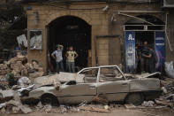 People stand next to a car damaged by Tuesday's explosion in the seaport of Beirut, Lebanon, Friday, Aug. 7, 2020. Rescue teams were still searching the rubble of Beirut's port for bodies on Friday, nearly three days after the massive explosion sent a wave of destruction through Lebanon's capital. (AP Photo/Felipe Dana)