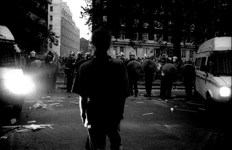 <span class="caption">A man stands in front of a line of riot police while protesting the Criminal Justice Act, 1994.</span> <span class="attribution"><span class="source">© Matthew Smith</span></span>