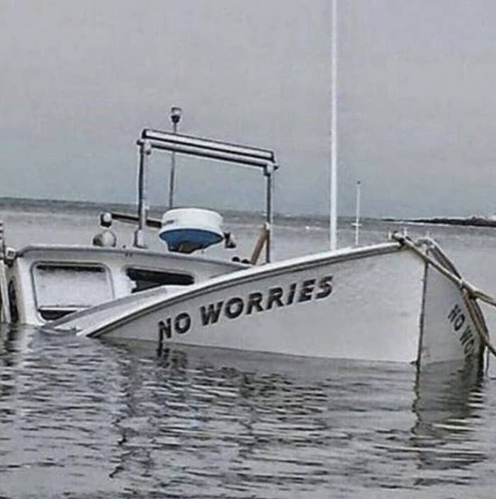 A partially submerged boat with the ironic name "NO WORRIES" visible on its side