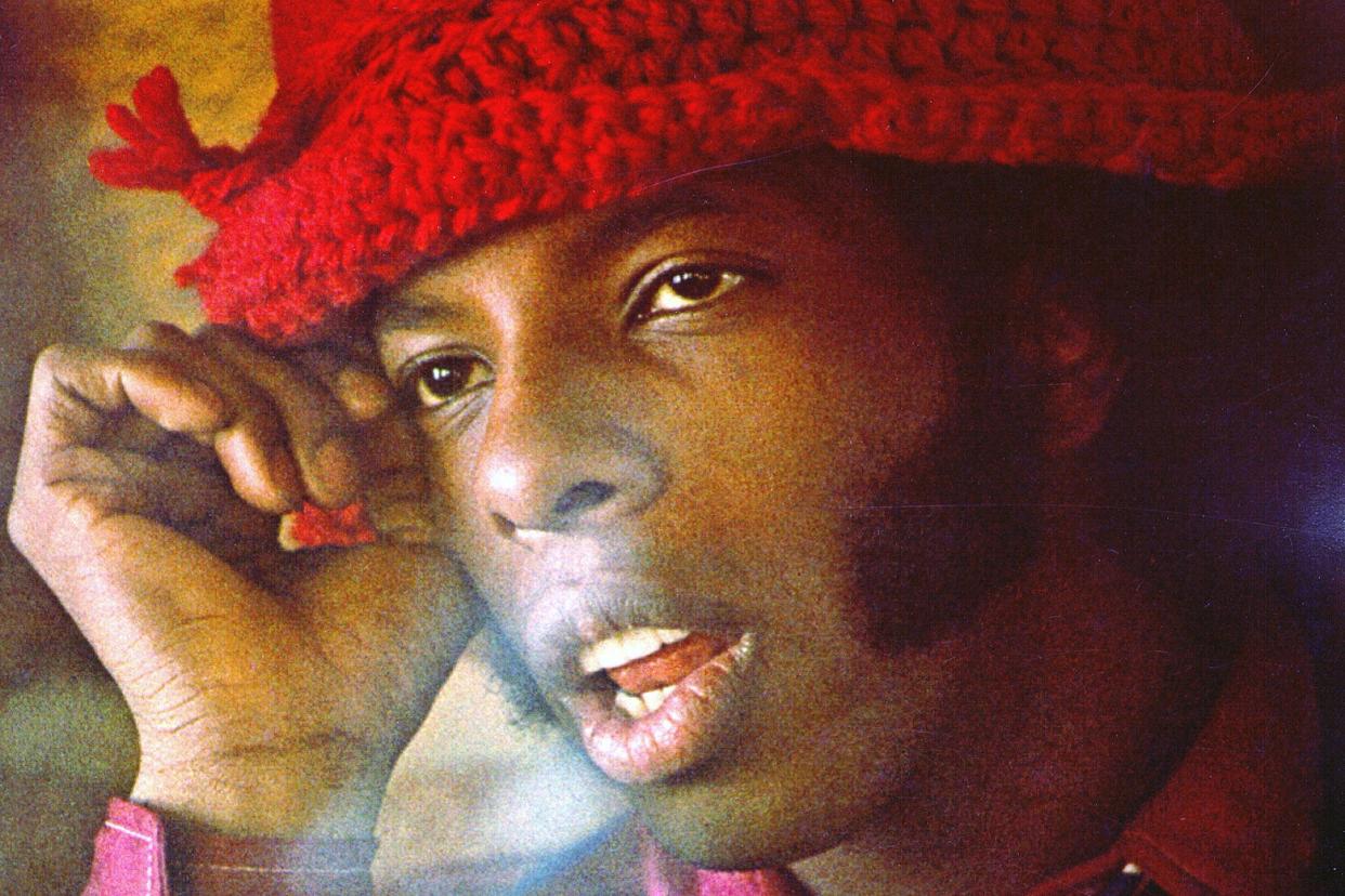 A close-up of Sly wearing a big red hat, looking sleepy, and exhaling smoke. 