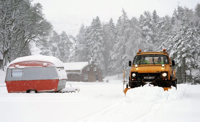 A snow plough passes an old caravan