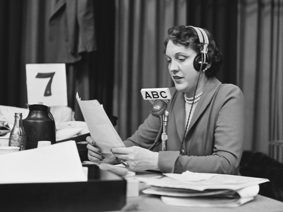 Black and white photo of Pauline reading a paper with headphones and speaking into a microphone.