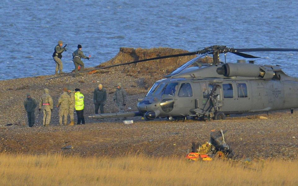 A Pave Hawk helicopter, military personnel and emergency services attend the scene of a helicopter crash on the coast near the village of Cley in Norfolk, eastern England