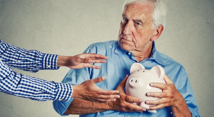 Older man clutching a piggy bank as someone tries to take it