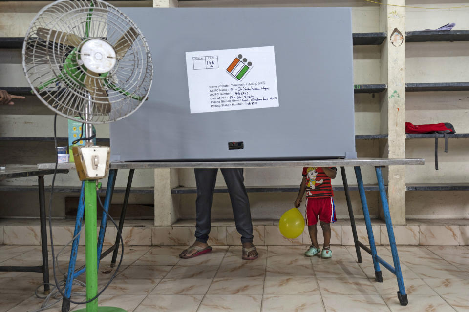 FILE- A child holding a balloon stands next to an adult casting his vote at a polling station during the first round of polling of India's national election in Chennai, southern Tamil Nadu state, Friday, April 19, 2024. (AP Photo/Altaf Qadri, File)