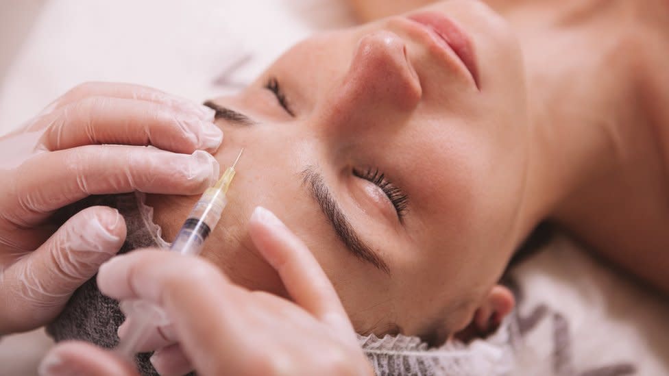 Top view close up of a woman receiving filler injections in forehead. Professional cosmetologist injecting hyaluronic acid into skin of female client