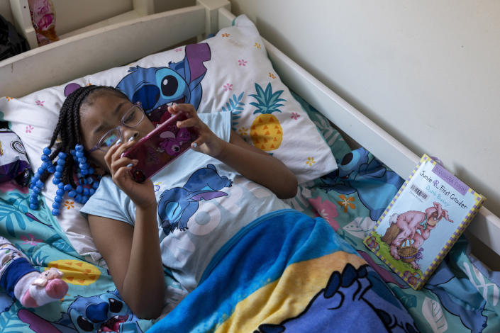 Ke'Arrah Jessie, 9, plays a game on her phone while resting in bed in Niagara Falls, N.Y., on Monday, April 3, 2023. Ke'Arrah was held back to repeat third grade after she had difficulty following along with online learning during the COVID-19 shutdown. (AP Photo/Lauren Petracca)