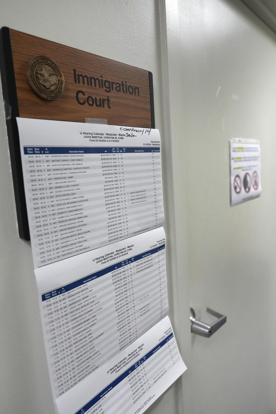 The hearing calendar for the day hangs next to a courtroom, Wednesday, Jan. 10, 2024, at an immigration court in Miami. Immigration courts are buckling under an unprecedented 3 million pending cases, most of them newly arrived asylum-seekers. The number of migrants trying to fight their deportation in front of a US judge has grown by 50% in less than a year. (AP Photo/Wilfredo Lee)