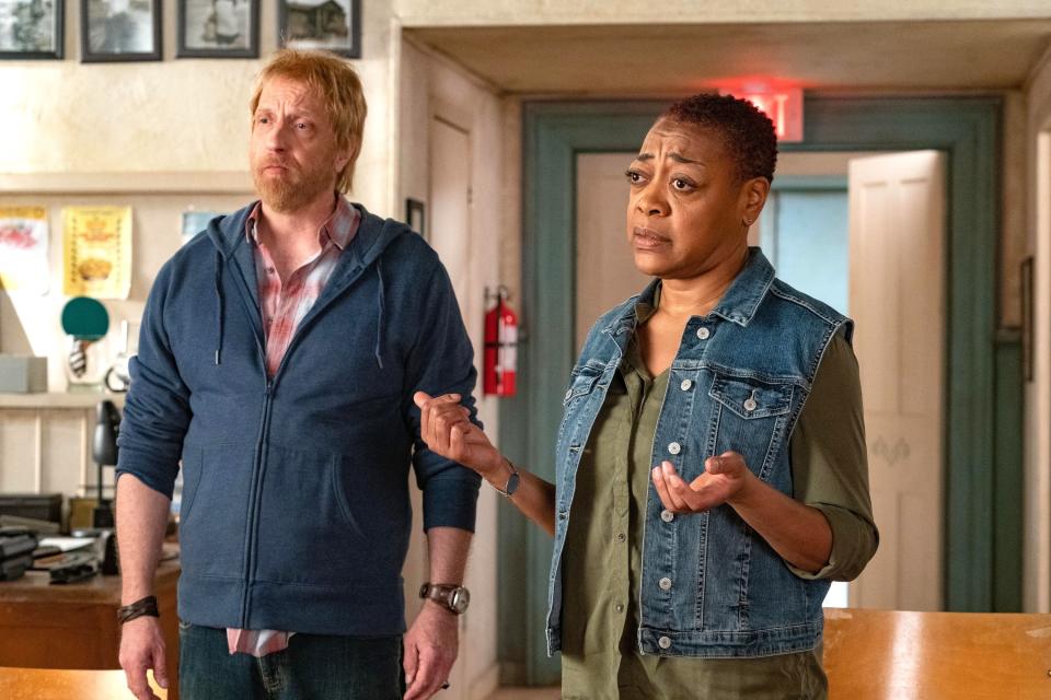 Two actors in a scene with one wearing a hoodie and the other a denim jacket, displaying concerned expressions