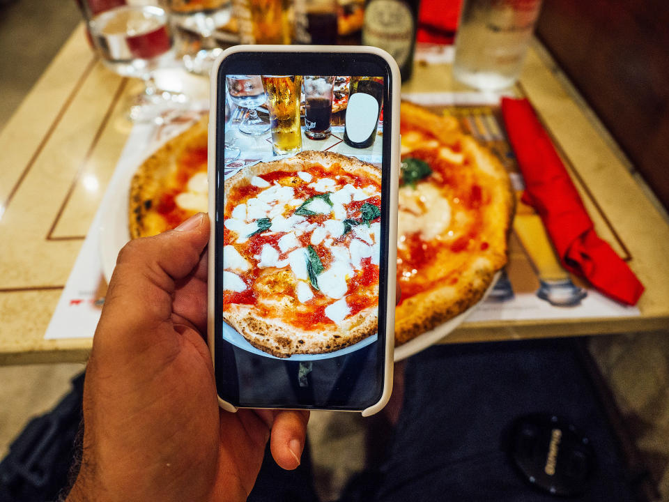 A man is taking a photo of his pizza in a restaurant. (FilippoBacci / Getty Images)