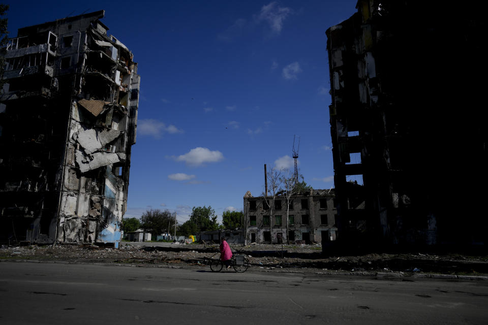 A woman rides a bicycle near buildings destroyed by attacks in Borodyanka, on the outskirts of Kyiv, Ukraine, Tuesday, May 31, 2022. (AP Photo/Natacha Pisarenko)
