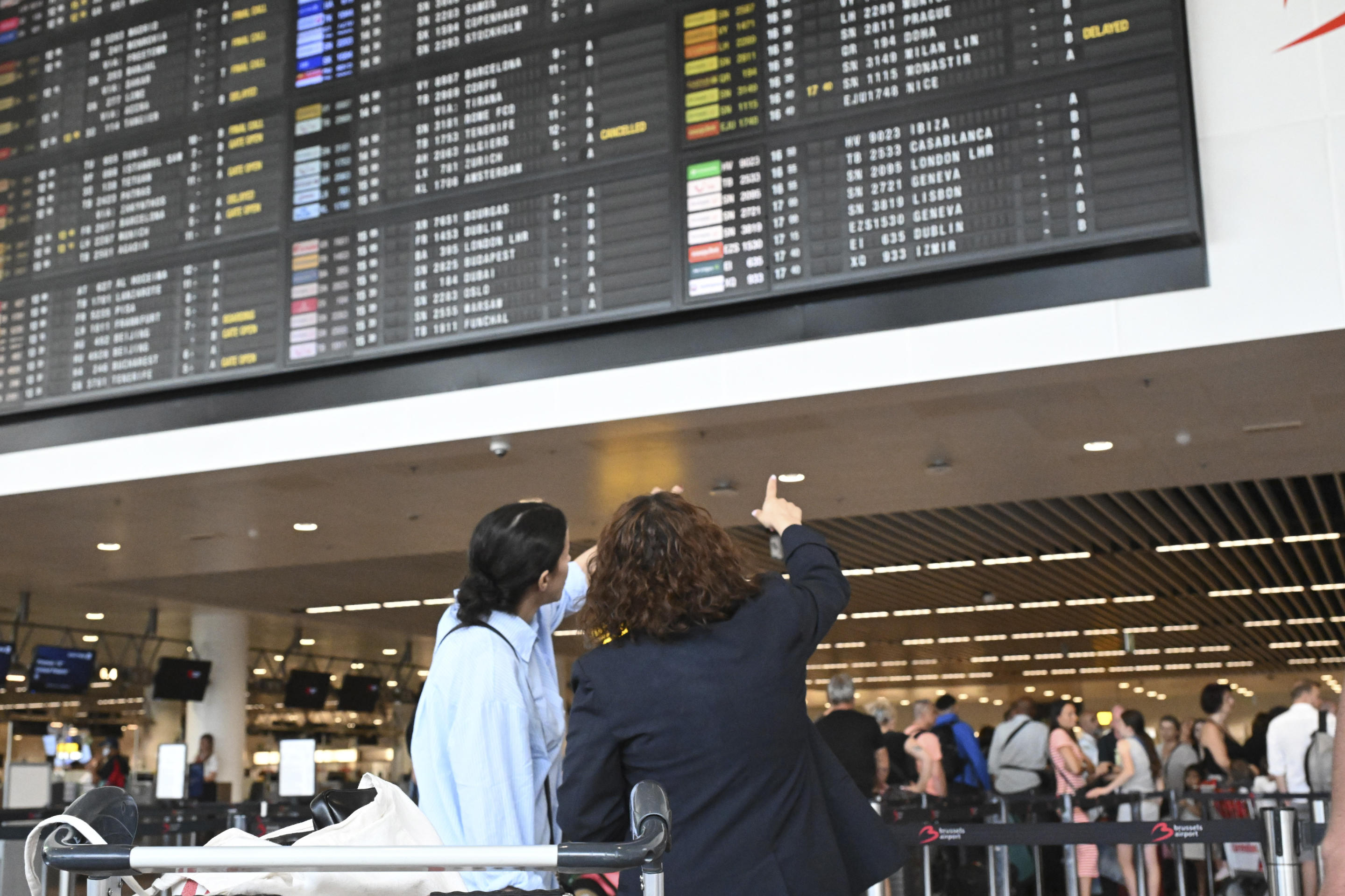 Travelers wait for information in front of a departure board at Brussels Airport.