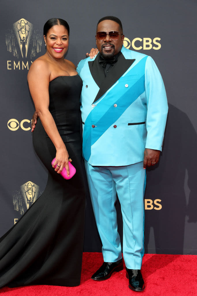 Cedric the Entertainer wears a brightly colored suit and Lorna Wells wears a strapless gown with a long train