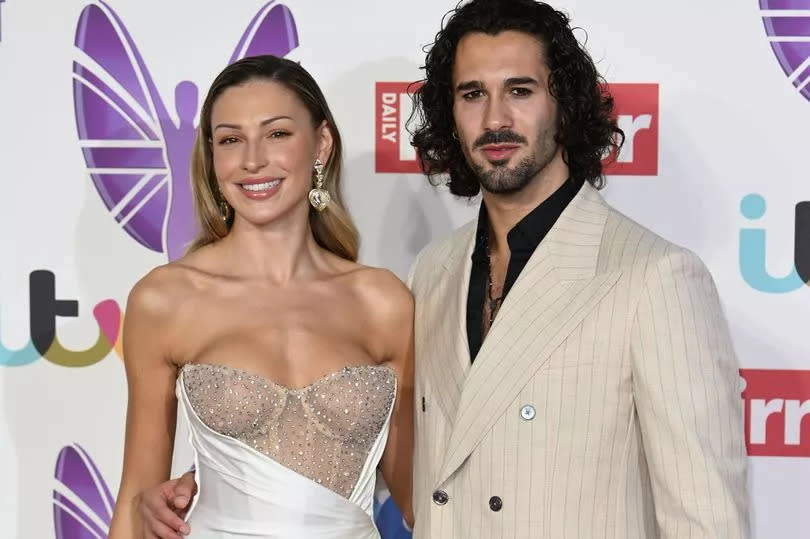 A woman in a strapless dress and a man in a beige jacket stand together