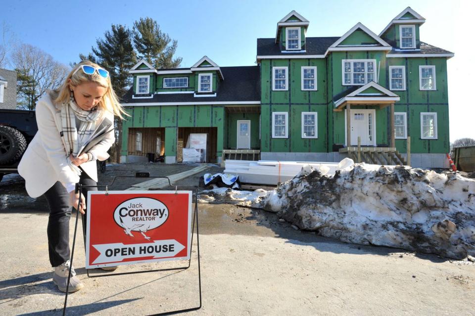 Real estate agent Alison Sheerin places an open house sign in front of a home under construction in the Curtis Estates in Scituate on Saturday, Feb. 12, 2022.