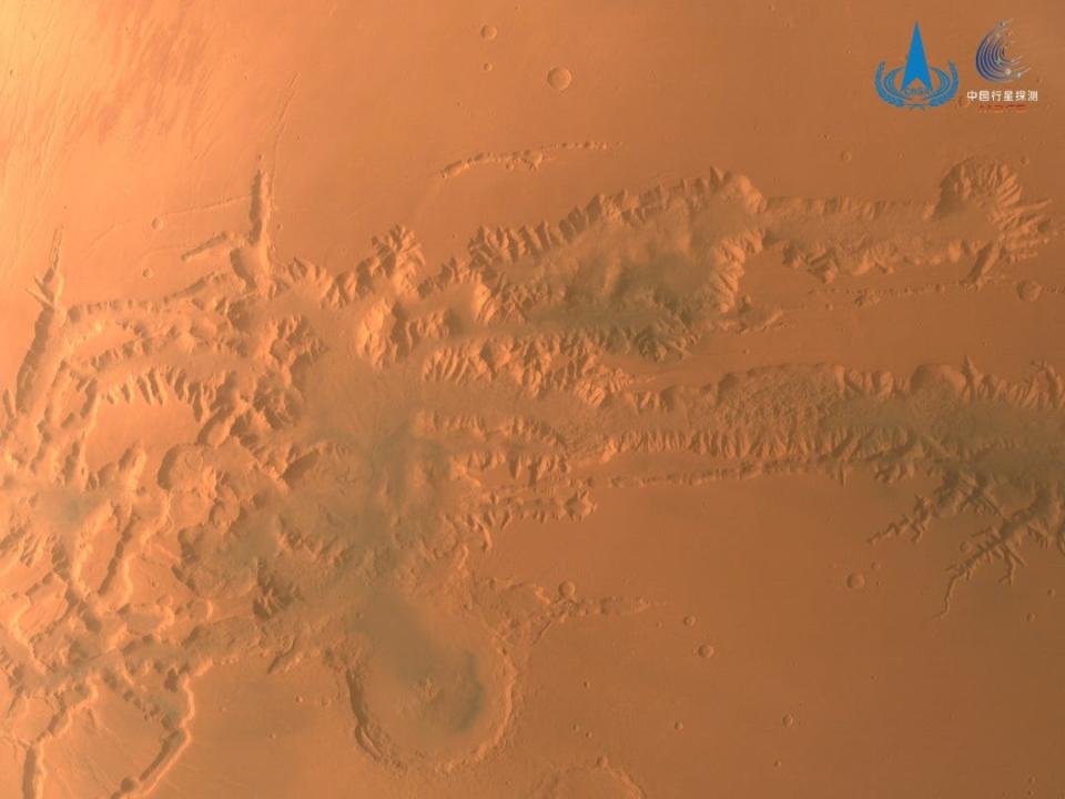 top-down space view of canyon cutting across orange mars landscape