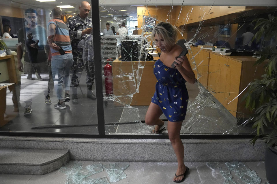 A bank employee exits the bank through a window broken by attackers, in Beirut, Lebanon, Wednesday, Sept. 14, 2022. An armed woman and a dozen activists broke into a Beirut bank branch on Wednesday, taking over $13,000 from what she says were from her trapped savings. Lebanon's cash-strapped banks since 2019 have imposed strict limits on withdrawals of foreign currency, tying up the savings of millions of people. (AP Photo/Hussein Malla)