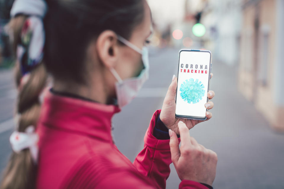 Woman using a phone with the coronavirus tracking app installed walking a city street