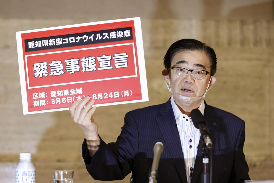 Aichi Gov. Hideaki Ohmura shows off a placard "State of Emergency" in Nagoya, Aichi prefecture, central Japan, Thursday, Aug. 6, 2020. Ohmura announced a state of emergency Thursday due to rising virus cases and asked businesses and people to curb their activities, especially during an upcoming holiday. Aichi prefecture has been seeing more than 100 new infections reported daily since mid-July after an extended period of zero new daily cases. (Kyodo News via AP)