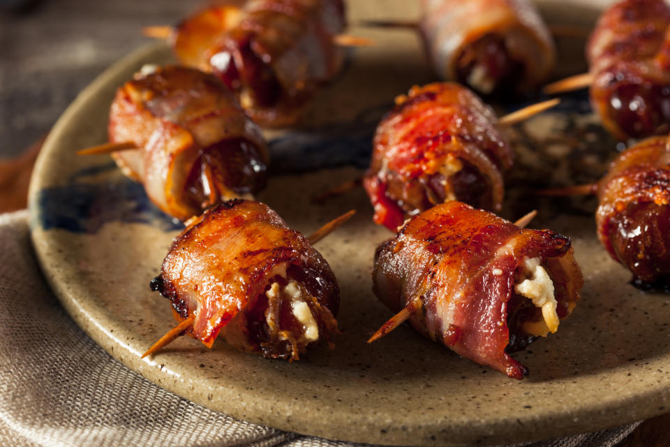 Close-up of bacon-wrapped stuffed dates with toothpicks on a ceramic plate