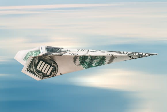 Paper plane folded from a hundred-dollar bill, on cloudy sky background.