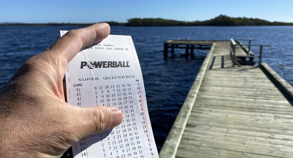 A man holding a winning Powerball ticket standing by the water