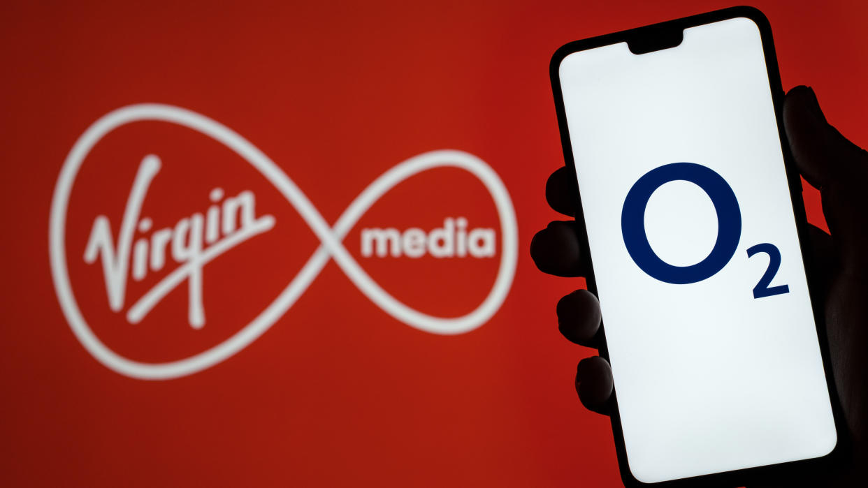  Person holding phone showing O2 logo in front of Virgin Media logo. 