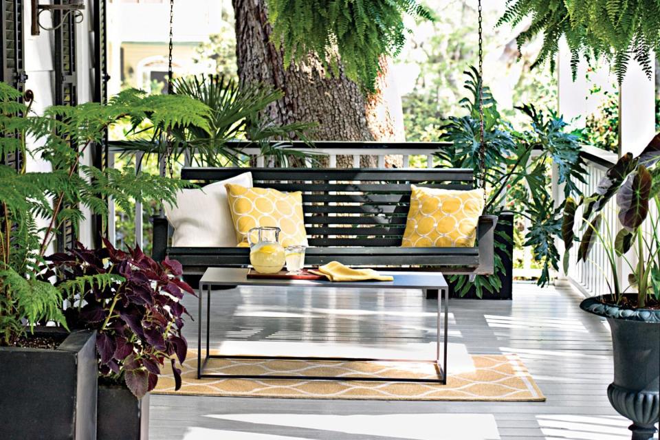 front porch with stylish swing, table with refreshments and surrounding plants and greenery