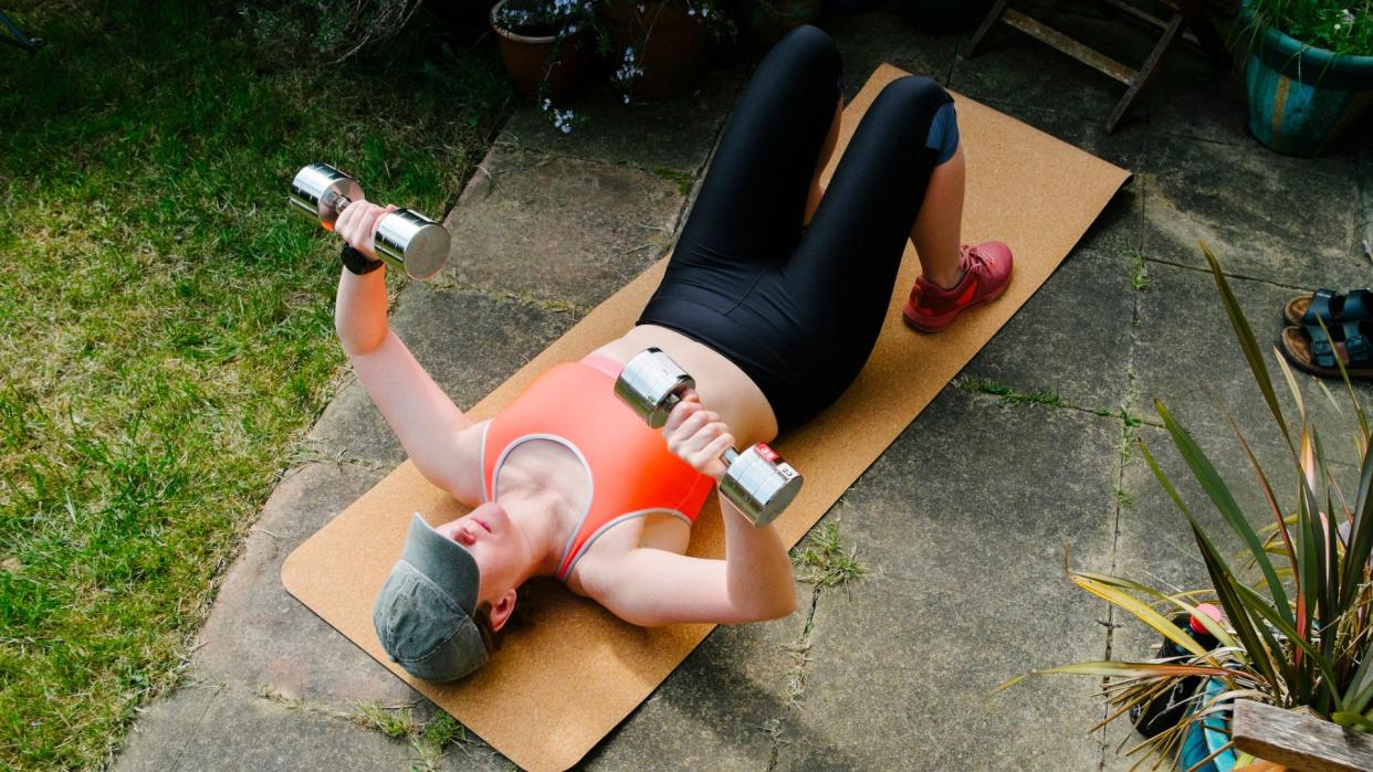  A woman performing the dumbbell floor press in a garden 