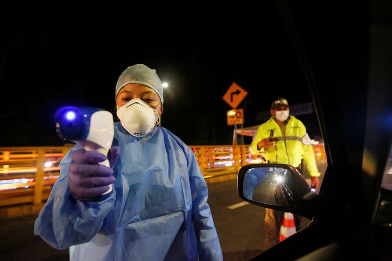 An Ecuadorian health official uses a thermal scanner on car passengers at Rumichaca International Bridge after Ecuador's government closed its borders to all foreign travelers due to the spread of the coronavirus disease, in Tulcan