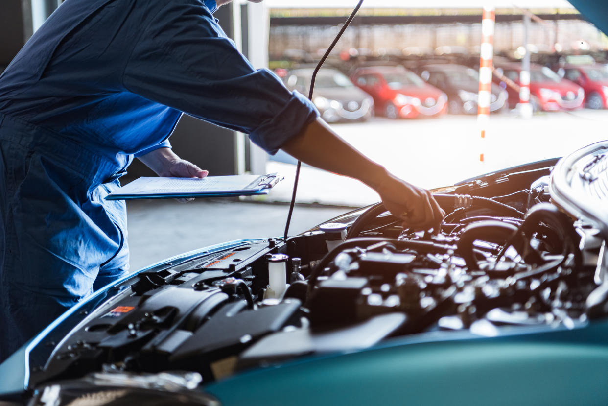 Car mechanic holding clipboard and checking to maintenance vehicle by customer claim order in auto repair shop garage. Engine repair service. People occupation and business job. Automobile technician