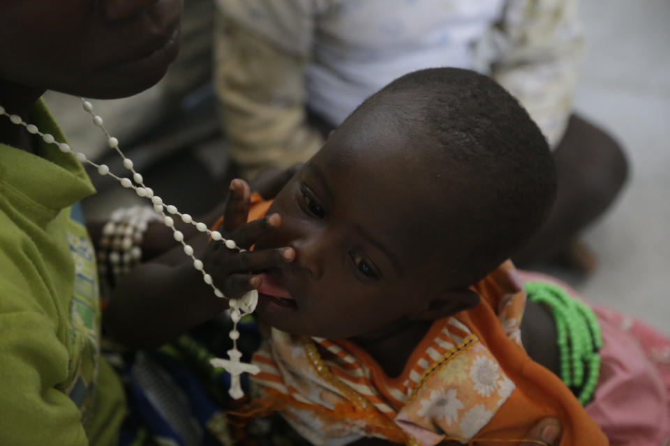 In this photo taken on Monday, Feb. 18, 2019, Rebecca Ishaku, a child displaced by Islamist extremist plays with a rosary as she is carried by her Mother Lucy Ishaku at Malkohi camp in Yola, Nigeria. For those who live in the makeshift camp for Nigerians who have fled Boko Haram violence, the upcoming presidential vote isn’t a topic of conversation, because nearly all are more worried about putting food on the table. (AP Photo/ Sunday Alamba)