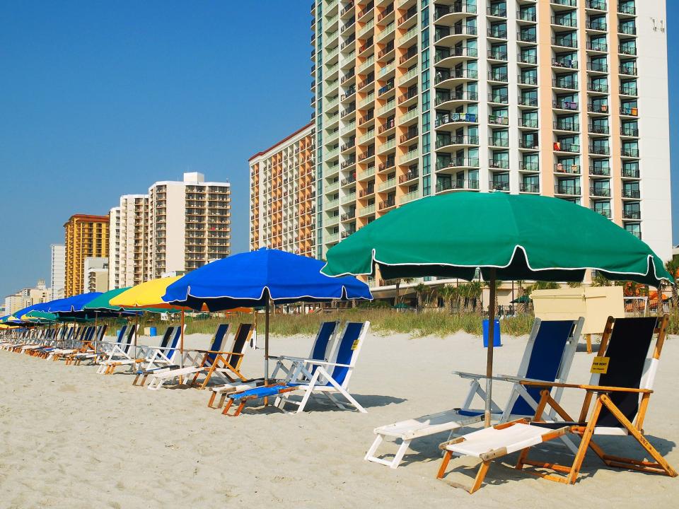 colorful beach umbrellas and lounge chairs lined up on a beach in front of condo buildings