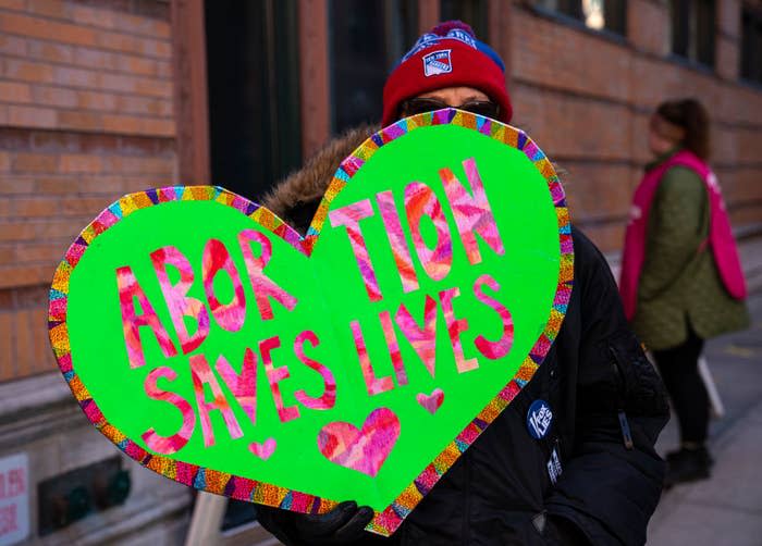 Person holding a large heart-shaped sign with the message "Abortion Saves Lives" surrounded by smaller hearts