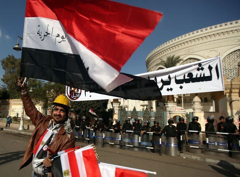 A street vendor waves th Egyptian flag outside the presidential palace guarded by riot police in Cairo. Egypt's powerful military has demanded the Islamist-led government and political foes start dialogue and warned it will not permit events to take a "disastrous" turn