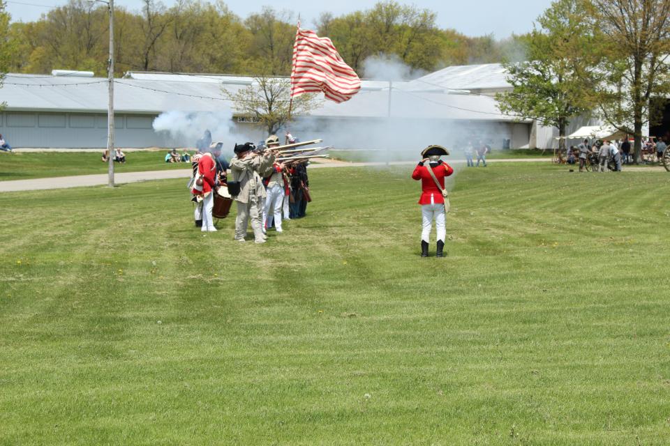 Men in artillery outfits fire off their musket rifles.