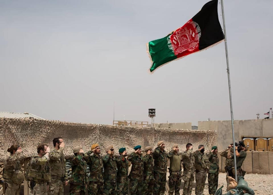 An Afghan flag flies as American and Afghan soldiers salute during a handover ceremony from the U.S. Army to the Afghan National Army, at Camp Anthonic, in Helmand province, southern Afghanistan, Sunday, May 2, 2021. (Afghan Ministry of Defense Press Office via AP)