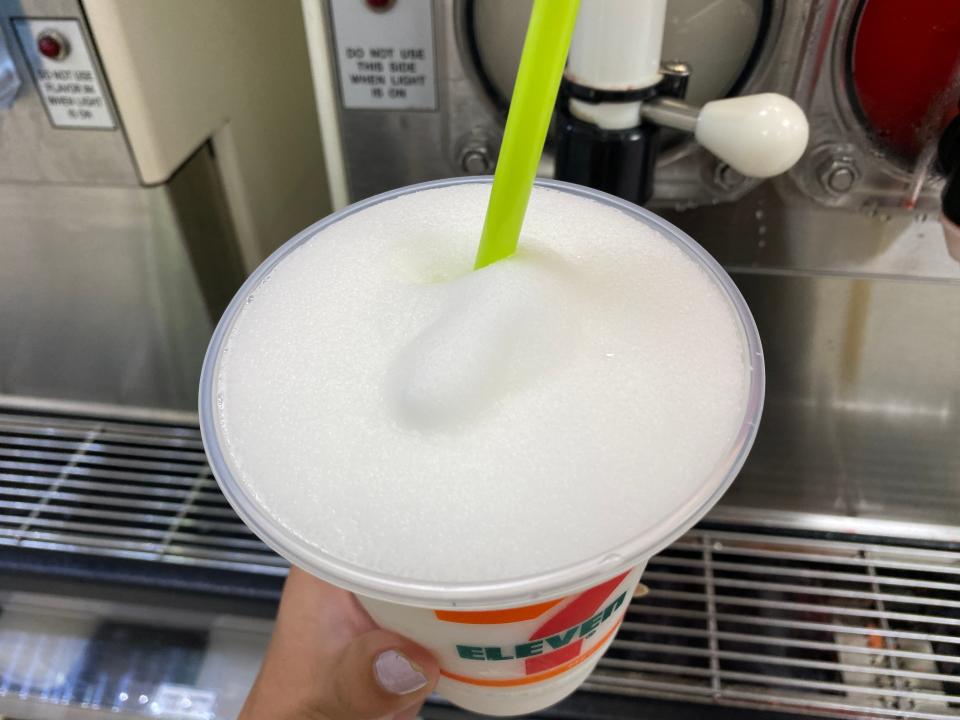 A hand holding a full 7/11 cup of pina colada slurpee