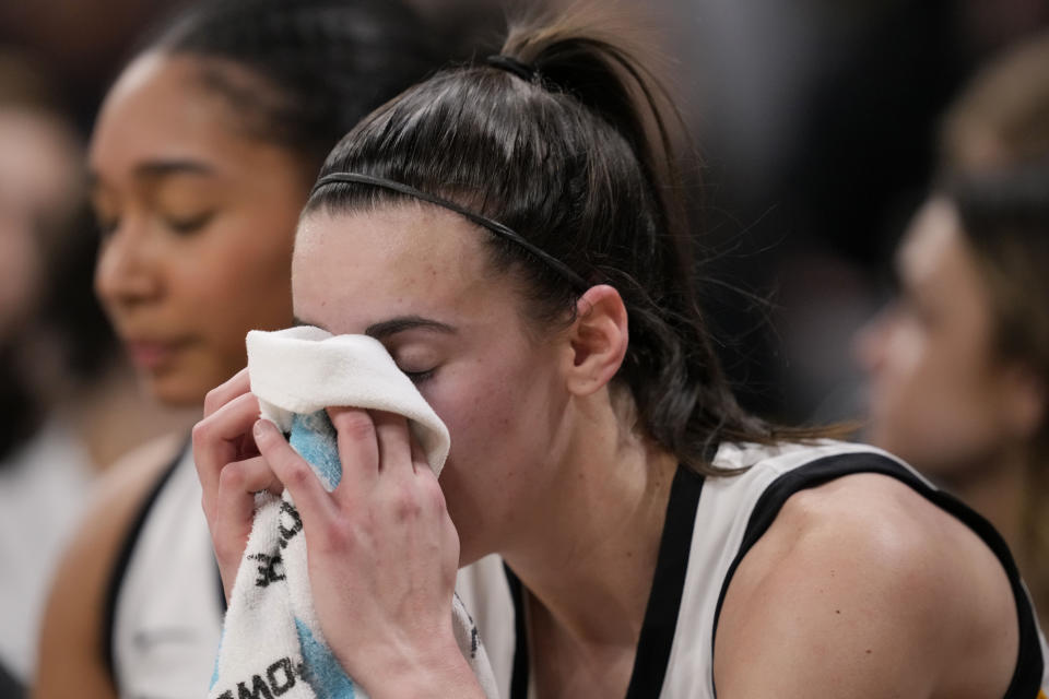 Iowa guard Caitlin Clark wipes her face on the bench in the final seconds of the the team's NCAA college basketball game against Michigan, Thursday, Feb. 15, 2024, in Iowa City, Iowa. Clark broke the NCAA women's career scoring record. (AP Photo/Matthew Putney)