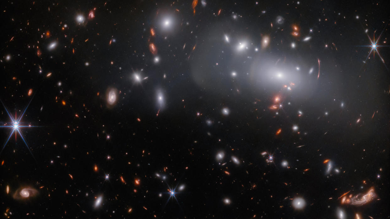  A large elliptical galaxy surrounded by many smaller similar galaxies as seen by the James Webb Space Telescope. 