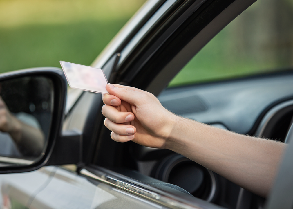 Person showing license through car window.